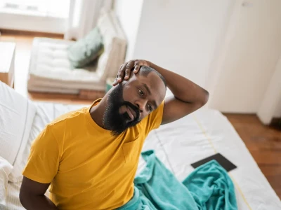 Homme assis dans son lit s'étirant pour soulager ses douleurs cervicales