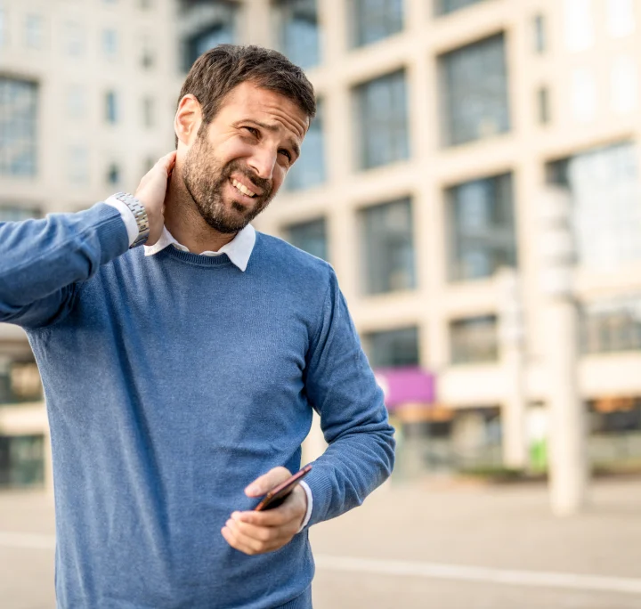 Un homme avec un pull bleu ayant des douleurs cervicales et essayant de les soulager avec sa main droite