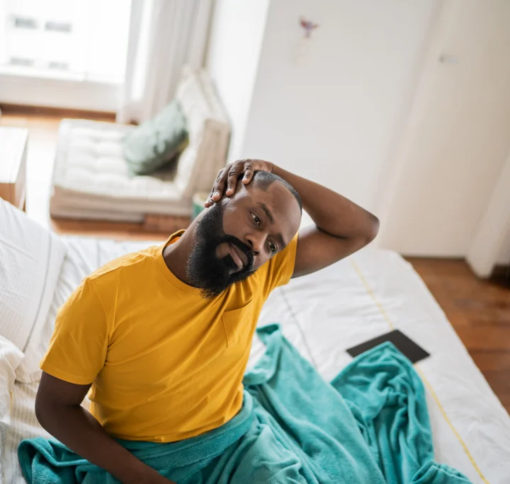 Homme assis dans son lit s'étirant pour soulager ses douleurs cervicales